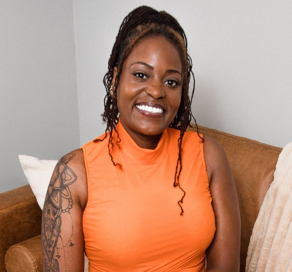 A woman is praying with her eyes closed in front of a wall of flowers.