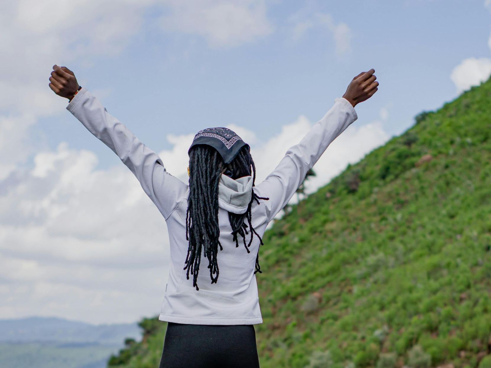 A woman is standing on top of a hill with her arms in the air.