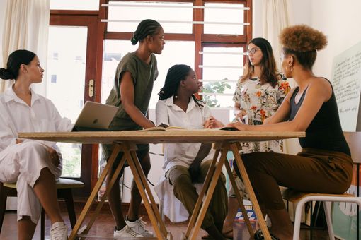 A group of women are sitting around a table having a meeting.