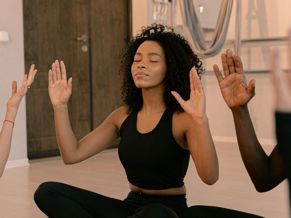 A woman is sitting in a lotus position with her eyes closed and her hands in the air.