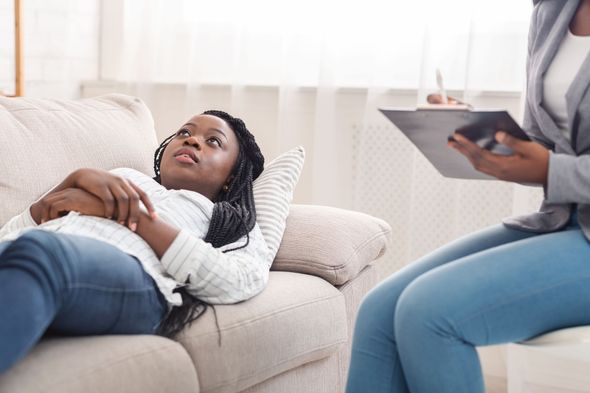 A woman is laying on a couch while a woman holds a clipboard.