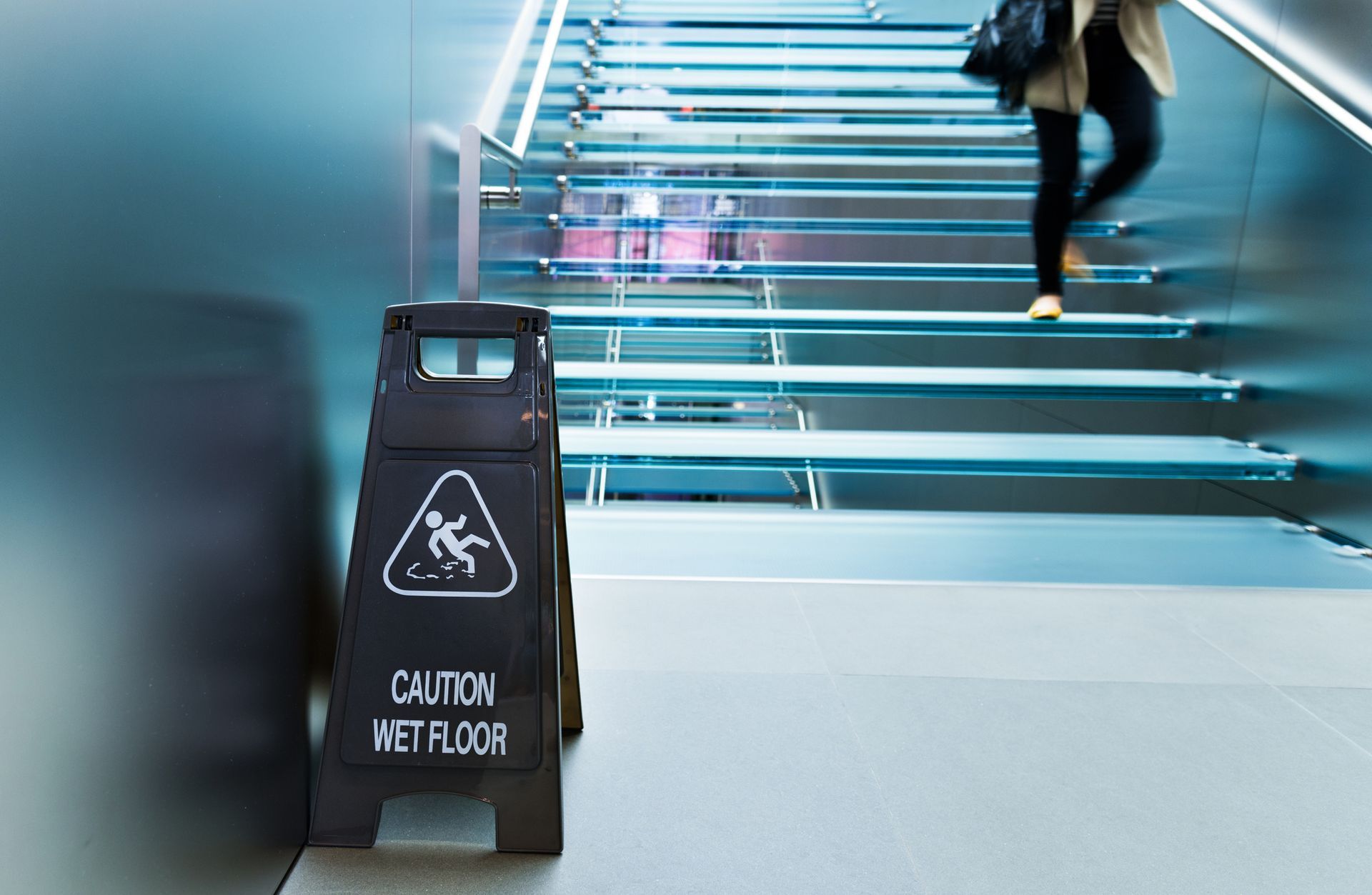 People walking down glass staircase with wet floor caution sign on floor. People walking down glass staircase with wet floor caution sign on floor.