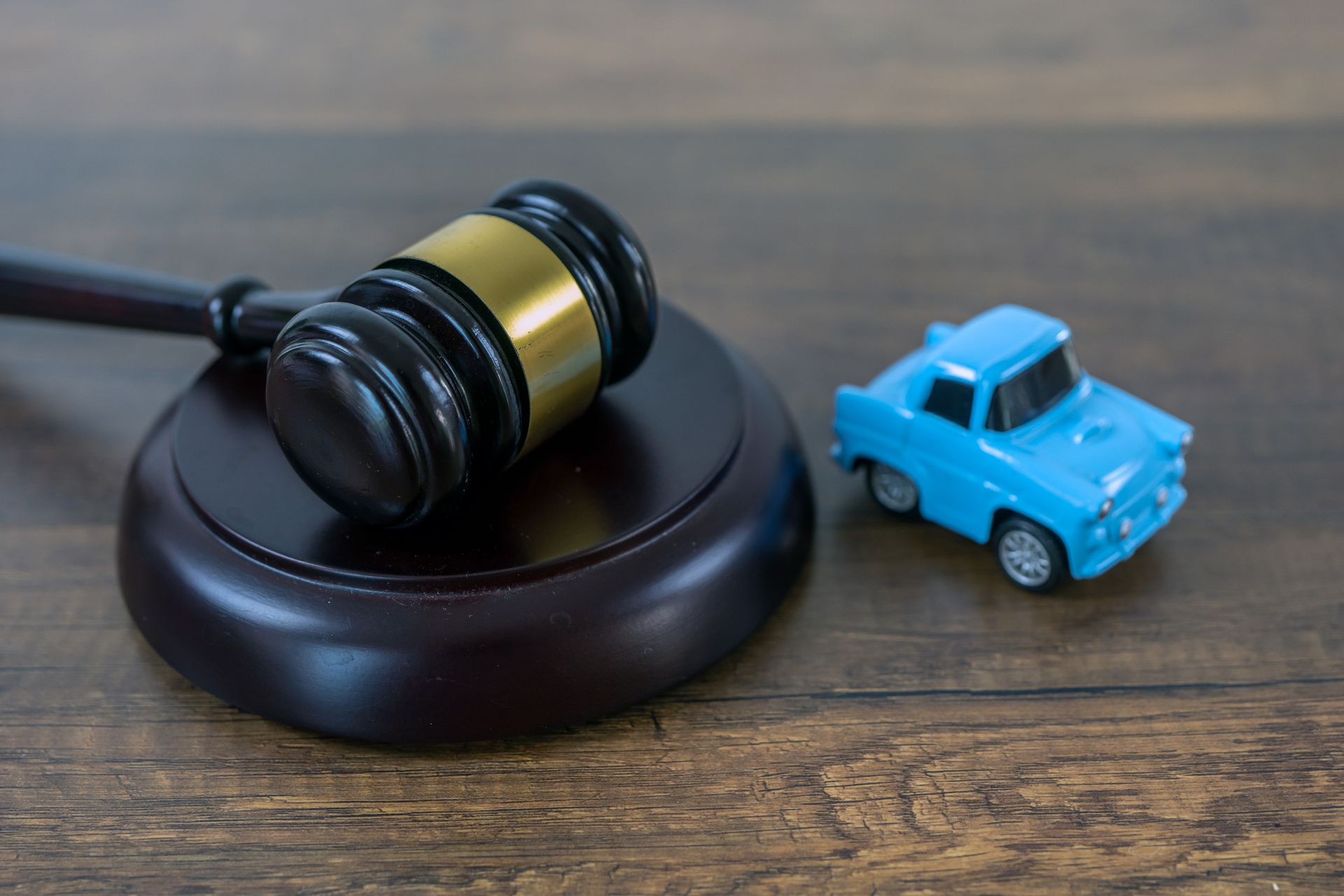 A blue toy car & a judge’s gavel on a table illustrate the concept of an auto accident attorney.