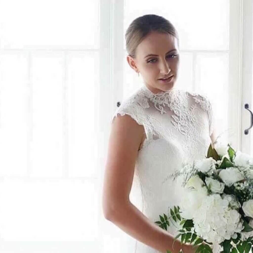 A bride in a white dress is holding a bouquet of white flowers.