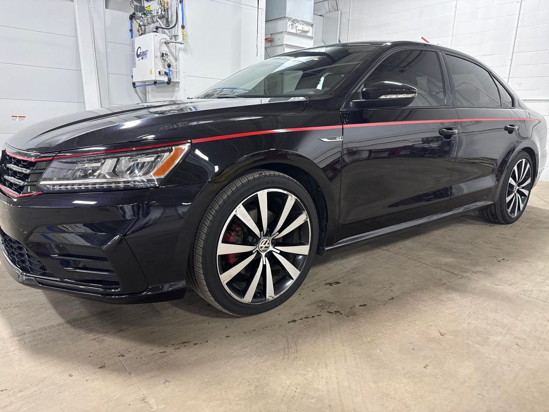 Black Volkswagen sedan with red stripe, custom wheels, in a garage.