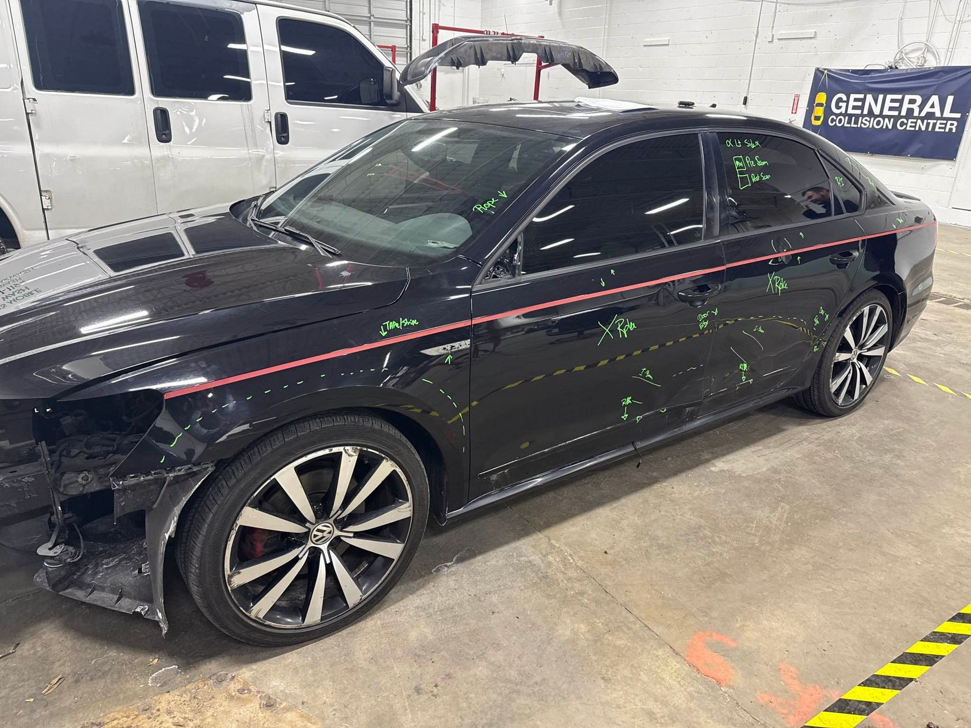Damaged black sedan in a repair shop, showing collision damage.
