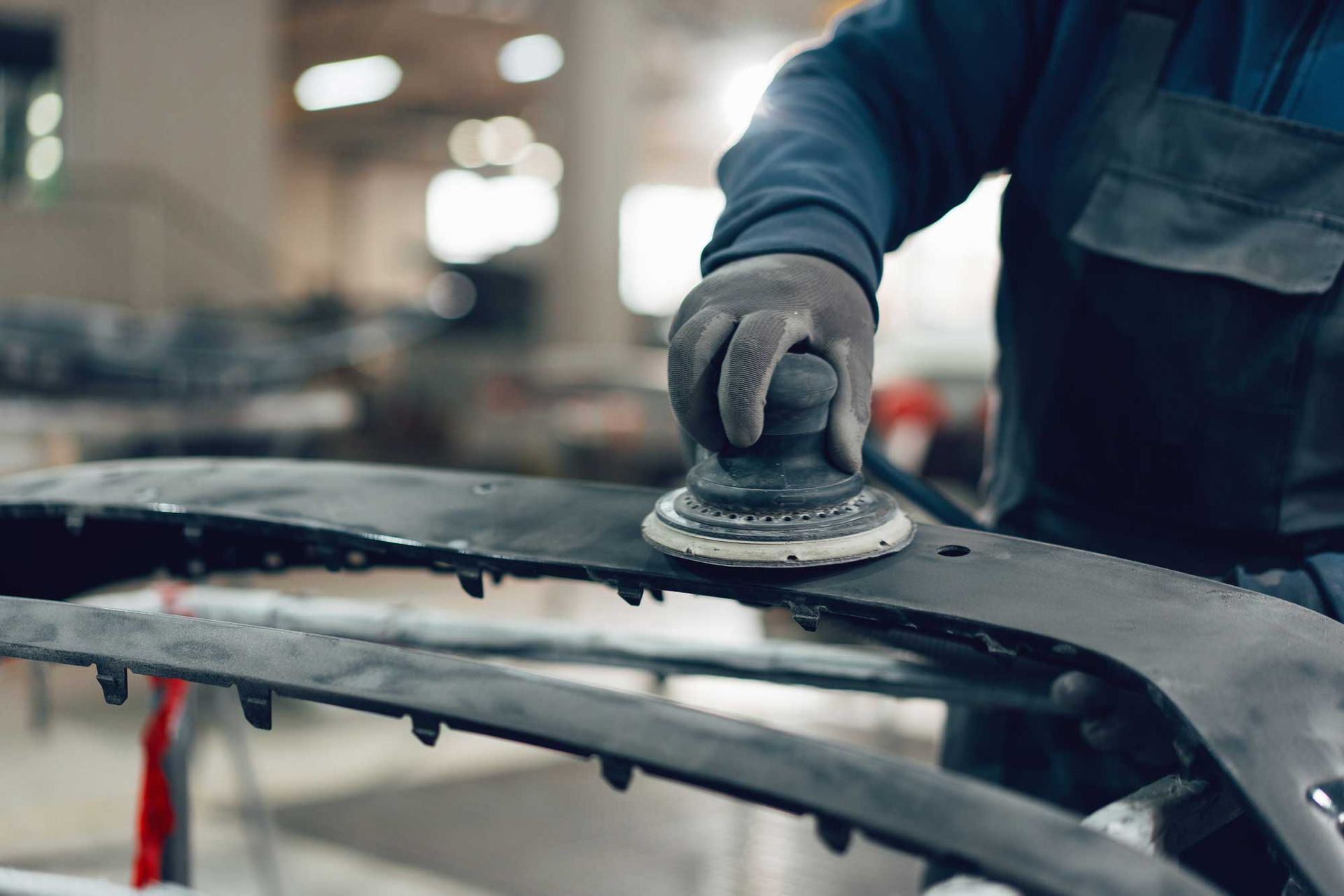 A person in gloves sands a car bumper in a workshop.