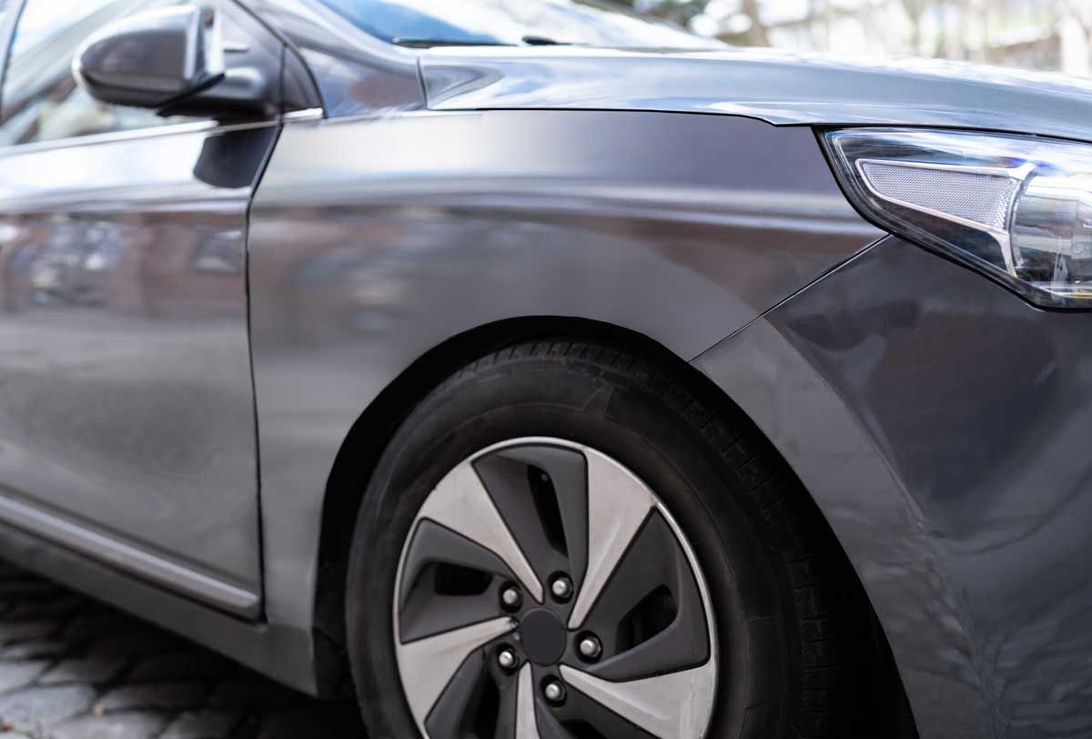 Close-up of a gray car's front fender and wheel, with a focus on the tire and hubcap.