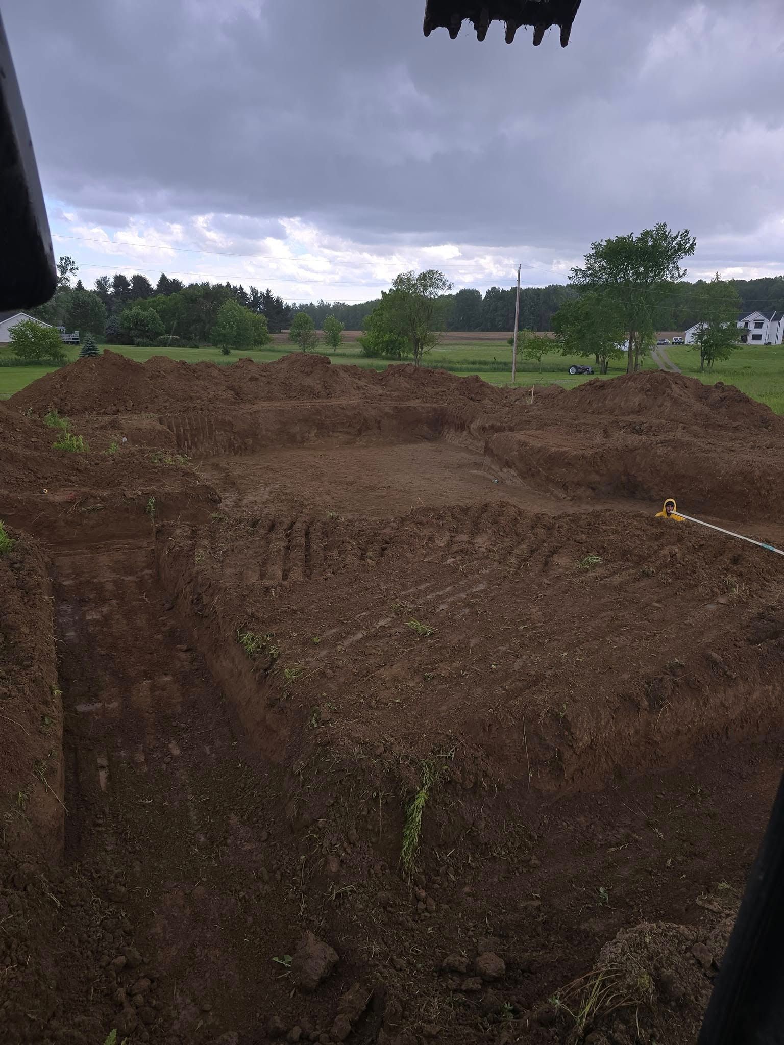 Excavated dirt in a field, viewed from heavy machinery cab under a cloudy sky.