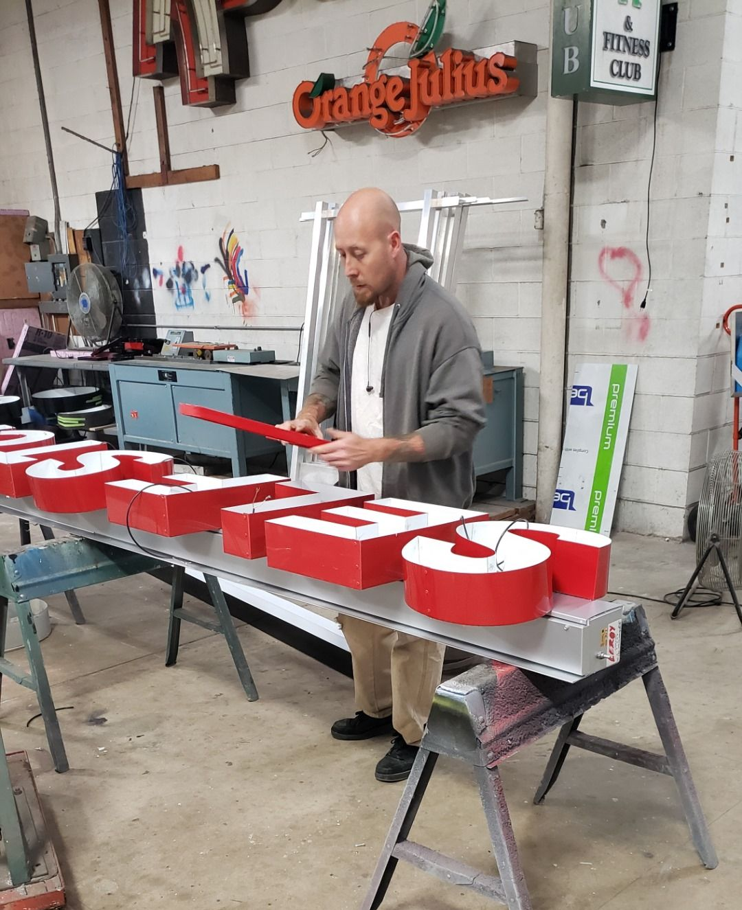 Man in workshop assembling red, lit sign letters. 