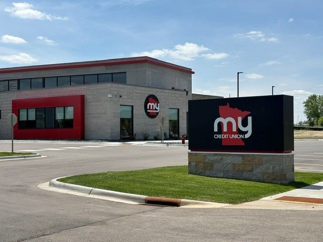 My credit union branch building with red trim and roadside sign under a blue sky