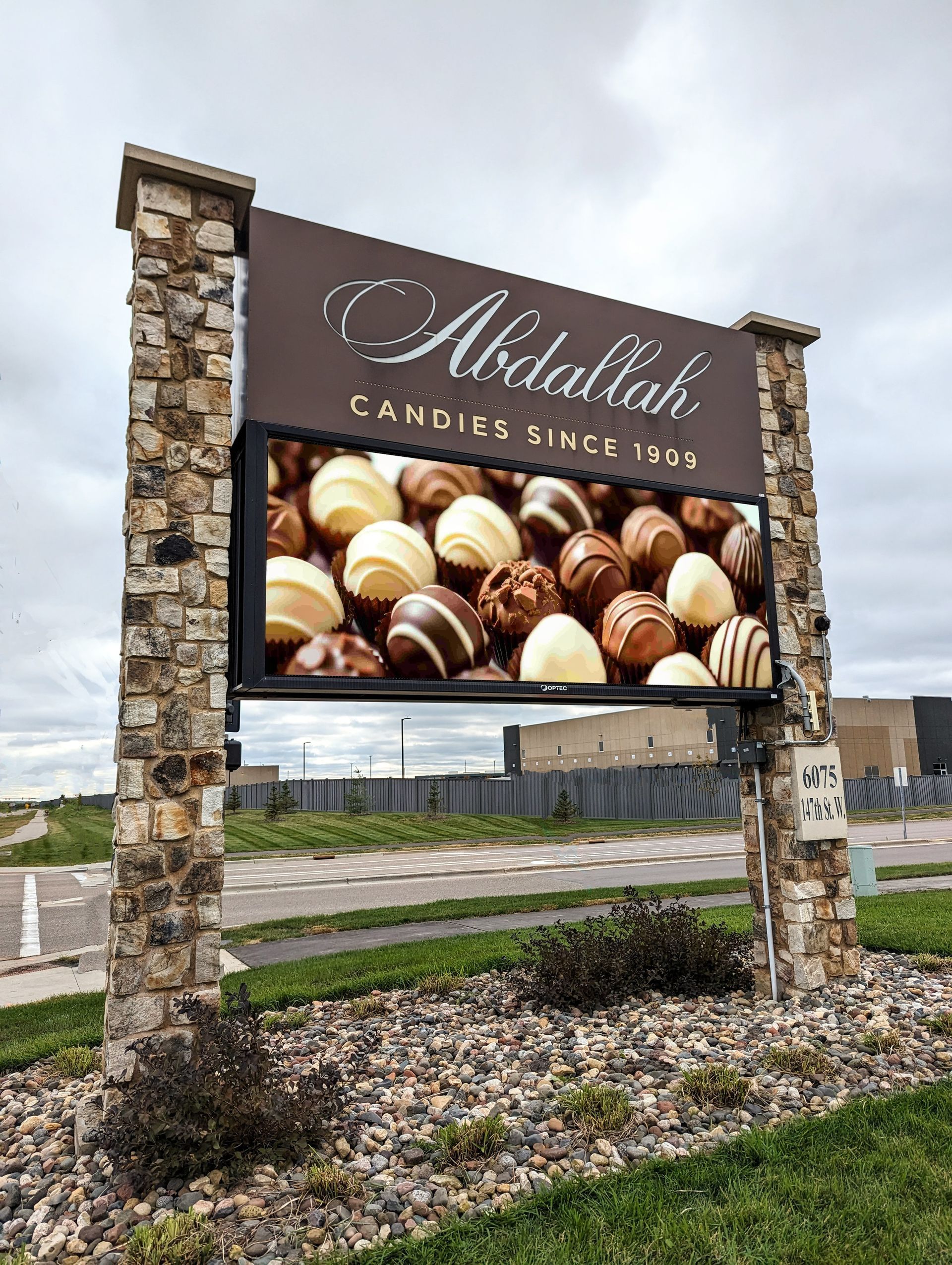 Sign for Abdullah Candies displaying chocolates. Brown stone posts and backdrop.