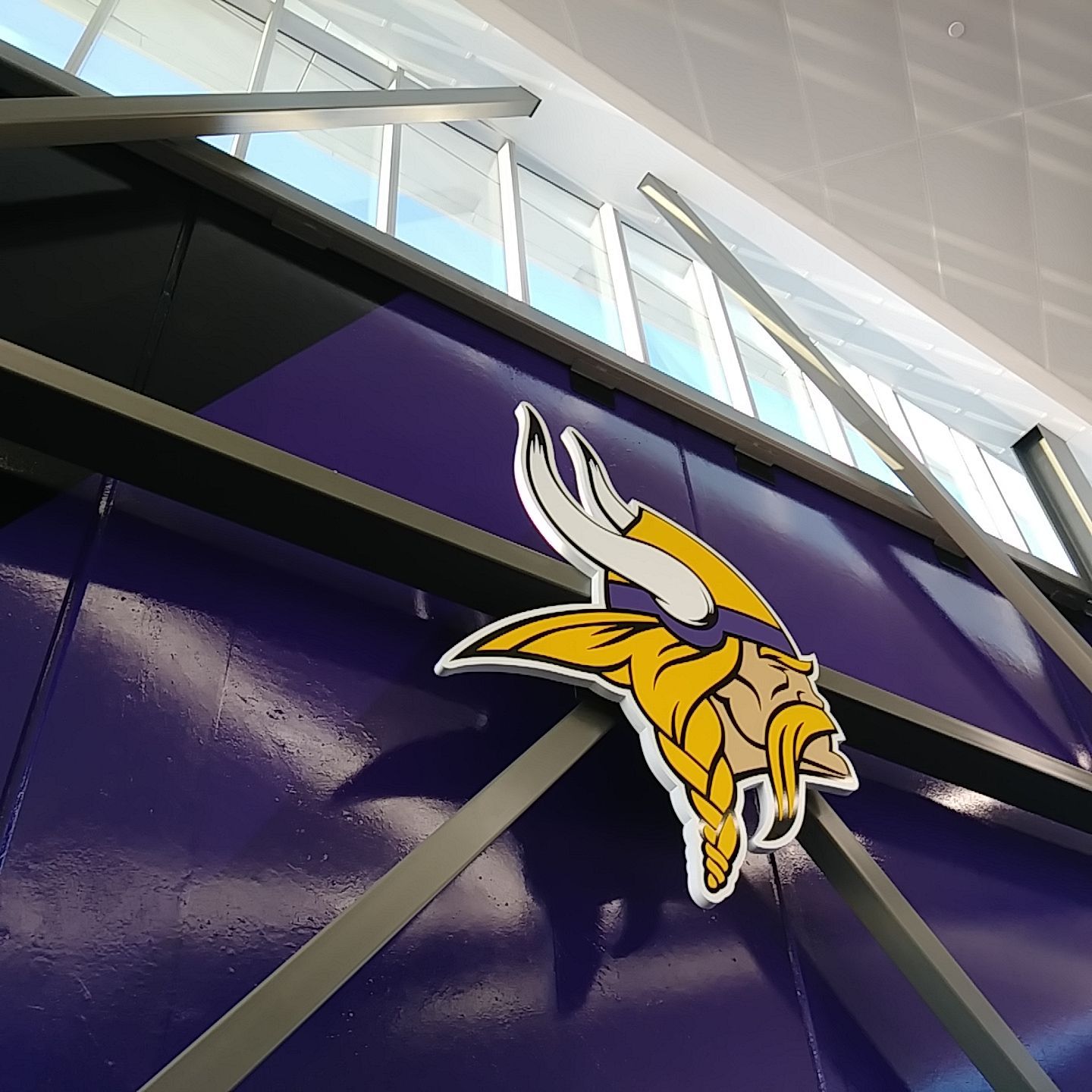 Minnesota Vikings logo on a purple wall with metal beams, near windows with natural light.