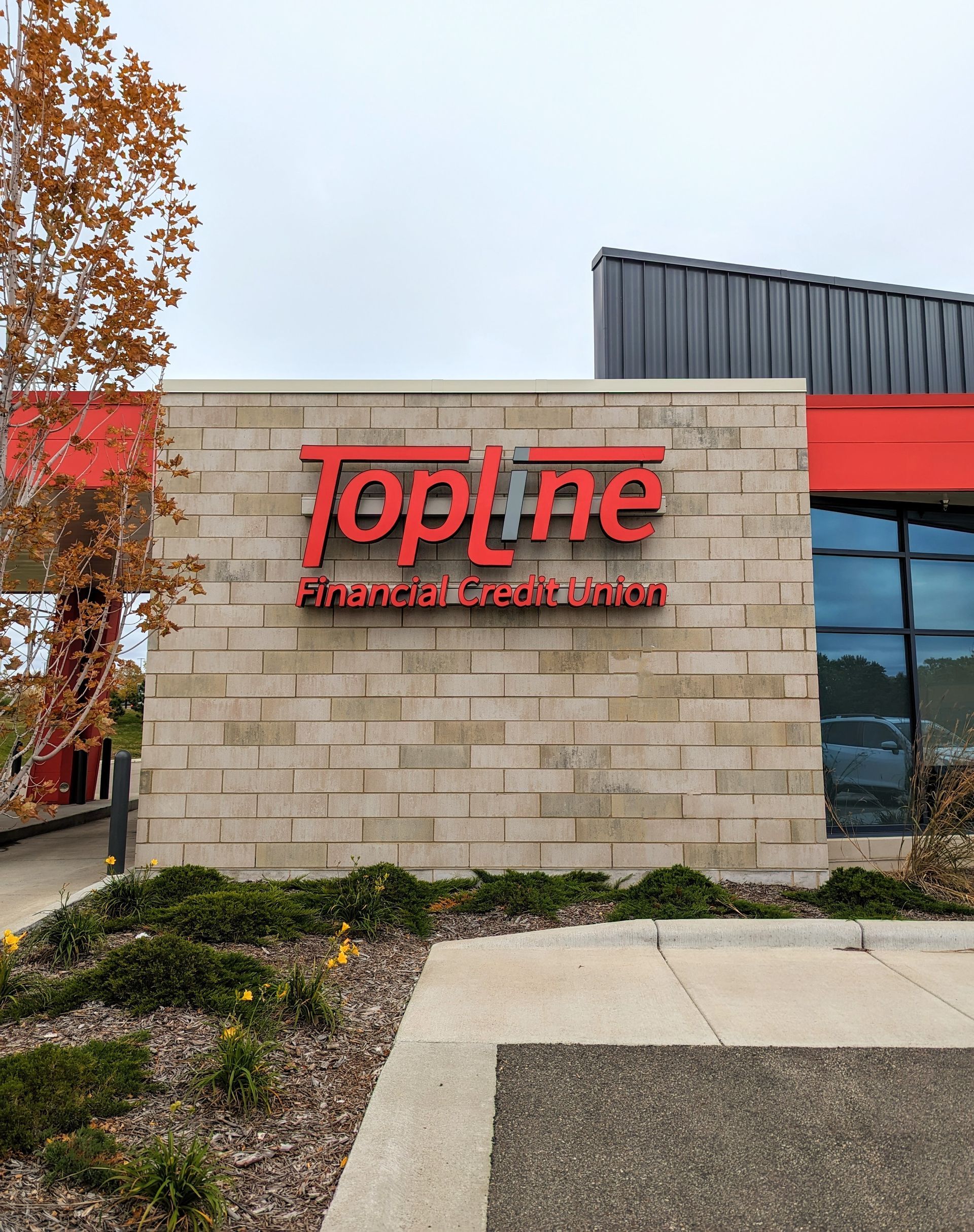 Topline store sign on tan stone wall, red logo, red building accent.