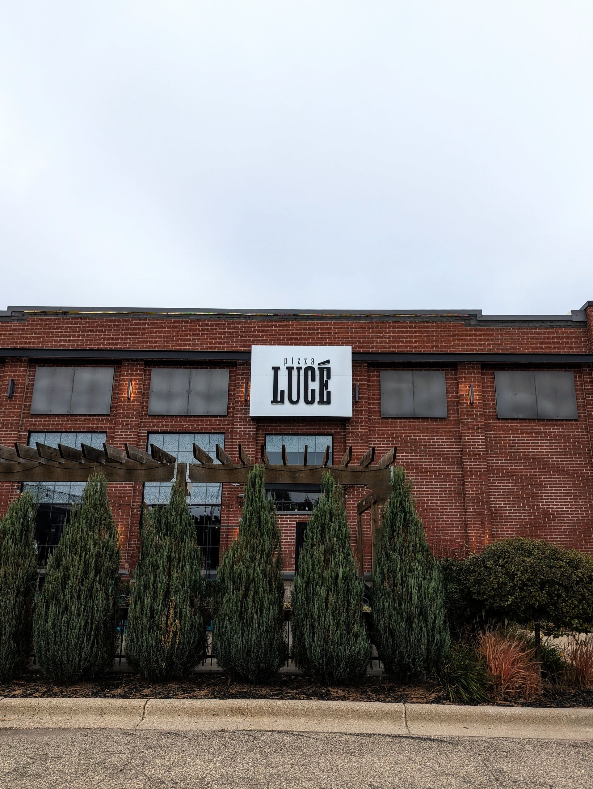 Red brick building with Luce sign. Windows boarded up. Evergreen trees in front. Cloudy sky. Red brick building with Luce sign. Windows boarded up. Evergreen trees in front. Cloudy sky.