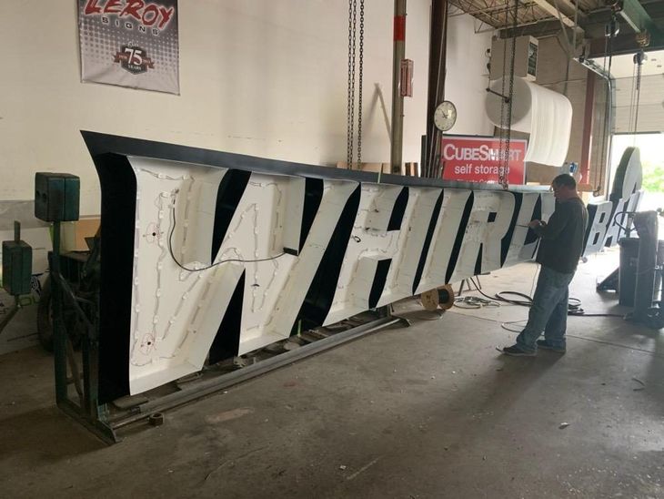 Man works on a large WHIRL sign with black trim and white letters inside a workshop. Man works on a large WHIRL sign with black trim and white letters inside a workshop.