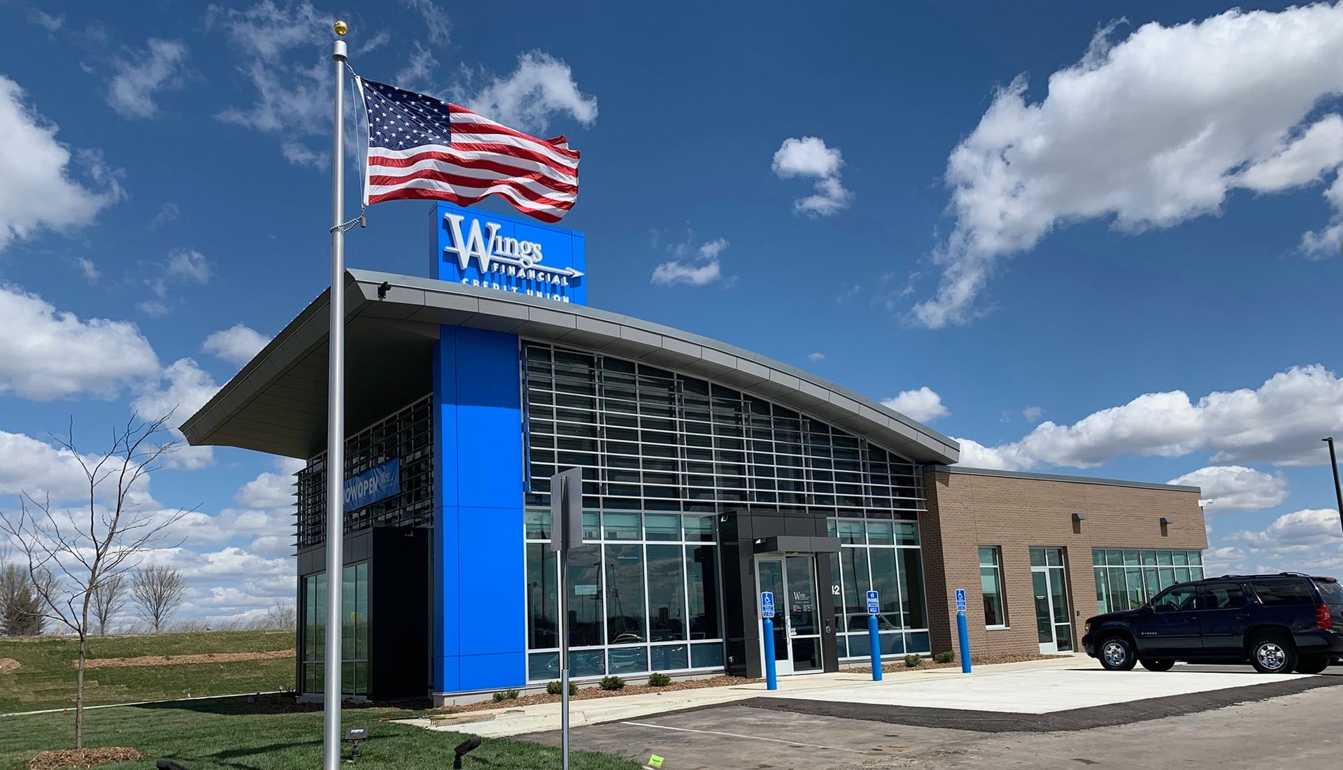 Bank building with an American flag waving in the wind. Modern design with blue accents, cloudy sky.