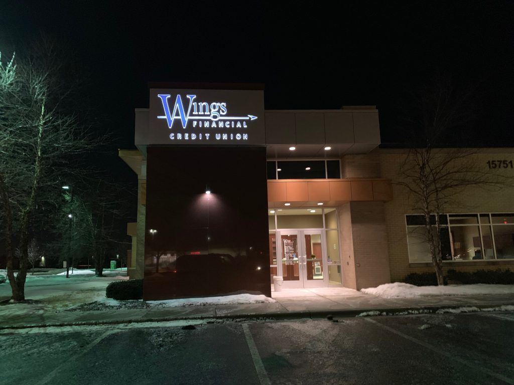 Night shot of Wings Financial Credit Union building, lit up, with snow on the ground.