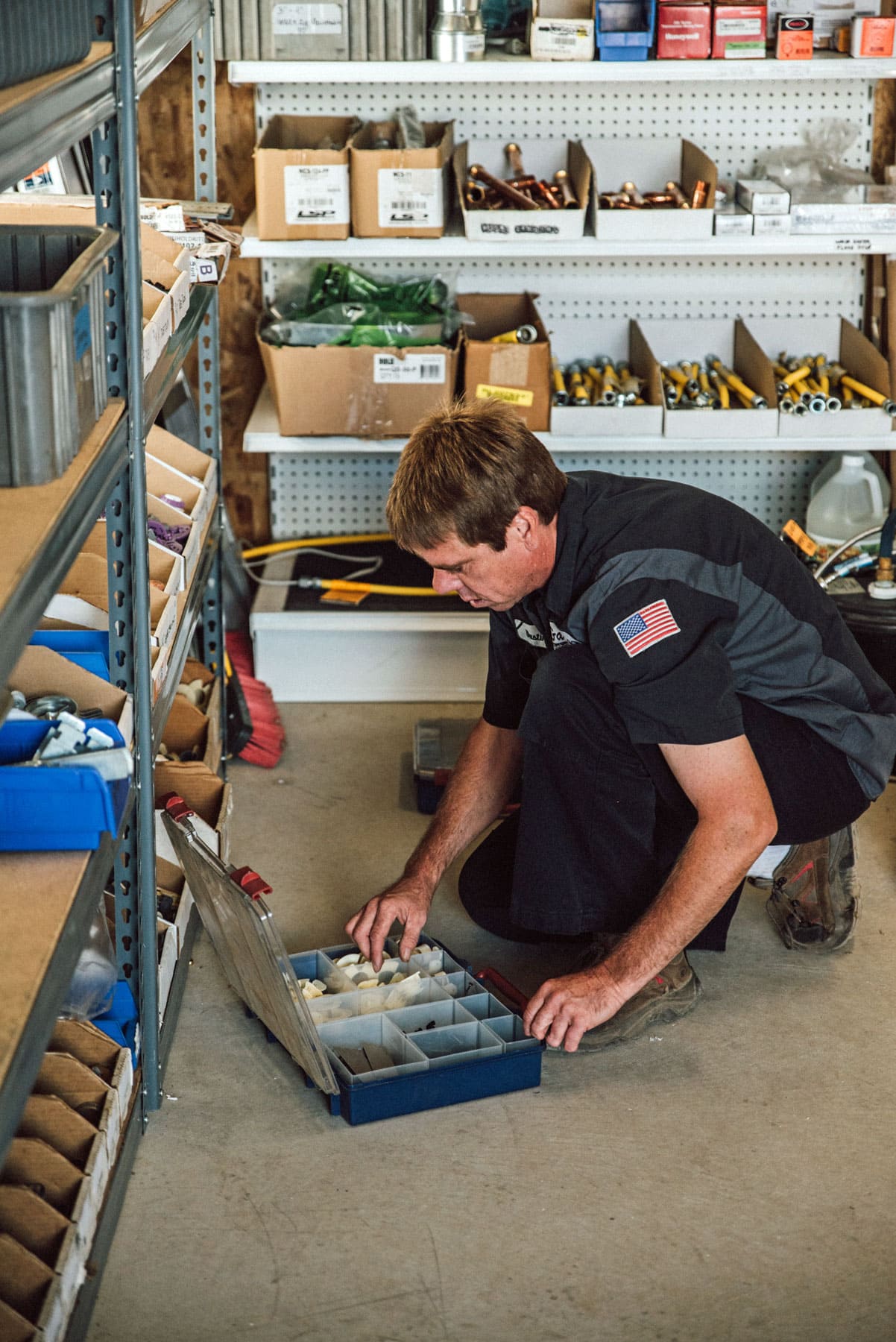 A man is kneeling down in a warehouse looking at a box of tools.
