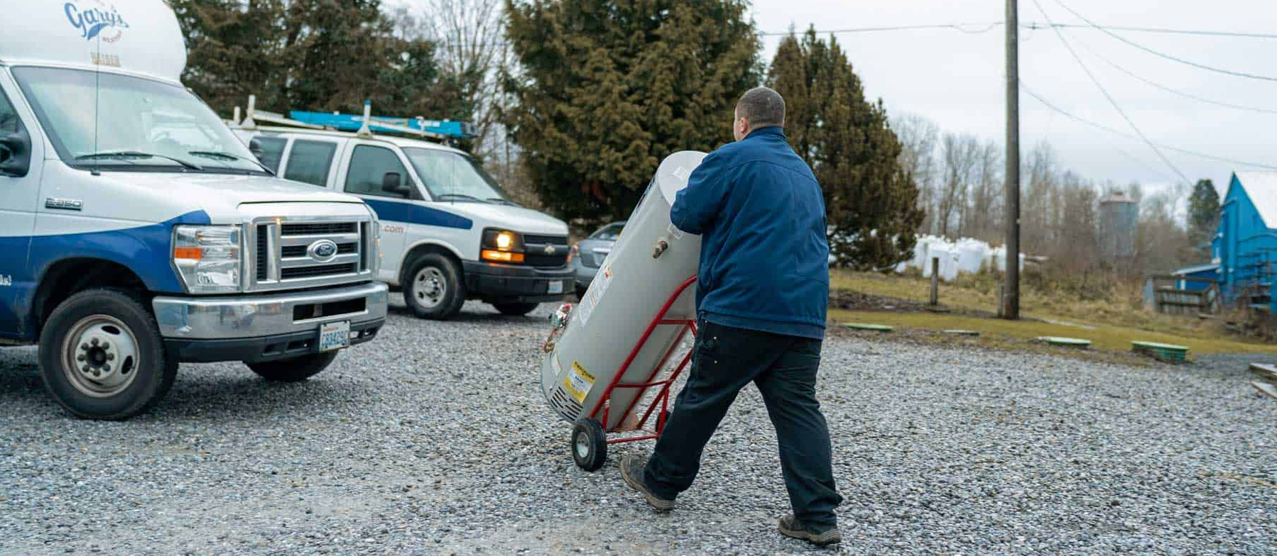 A man is pushing a water heater on a dolly in a parking lot.
