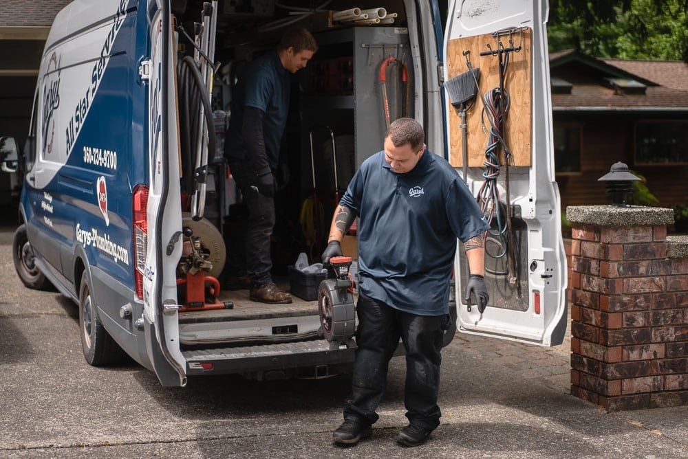 Two Gary's technicians unloading tools from a service van in front of a house. One carries a machine