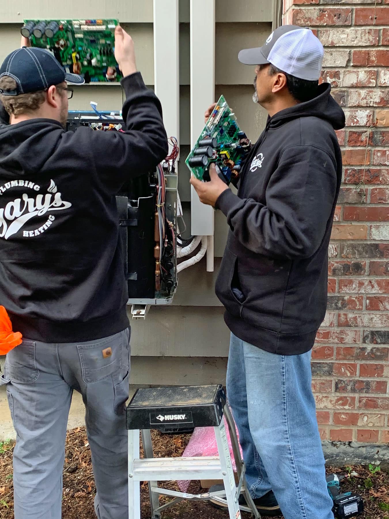 Two men are working on a electrical box outside of a brick building.