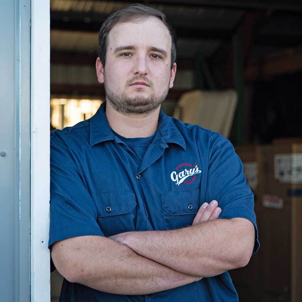 A man in a blue shirt is leaning against a wall with his arms crossed.