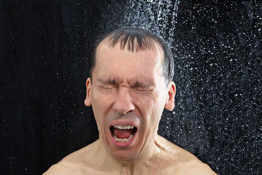 A man is taking a shower with his eyes closed and his mouth open