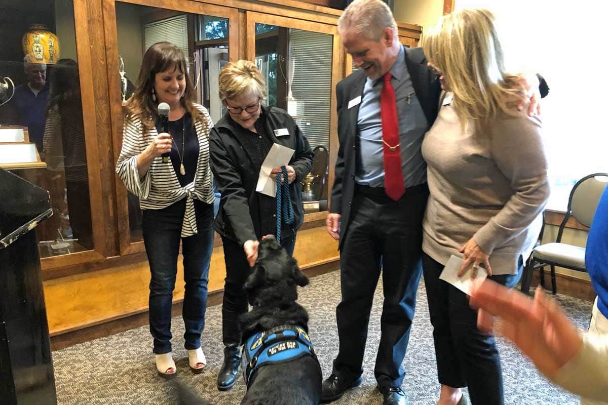 A group of people are standing around a dog in a room.