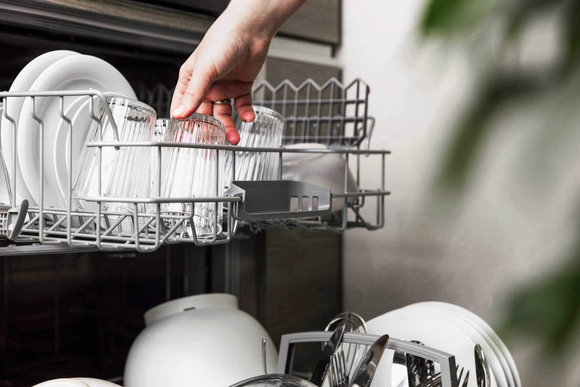 A person is putting a glass in a dishwasher.