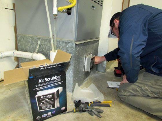 A man is kneeling down next to a box that says air scrubber