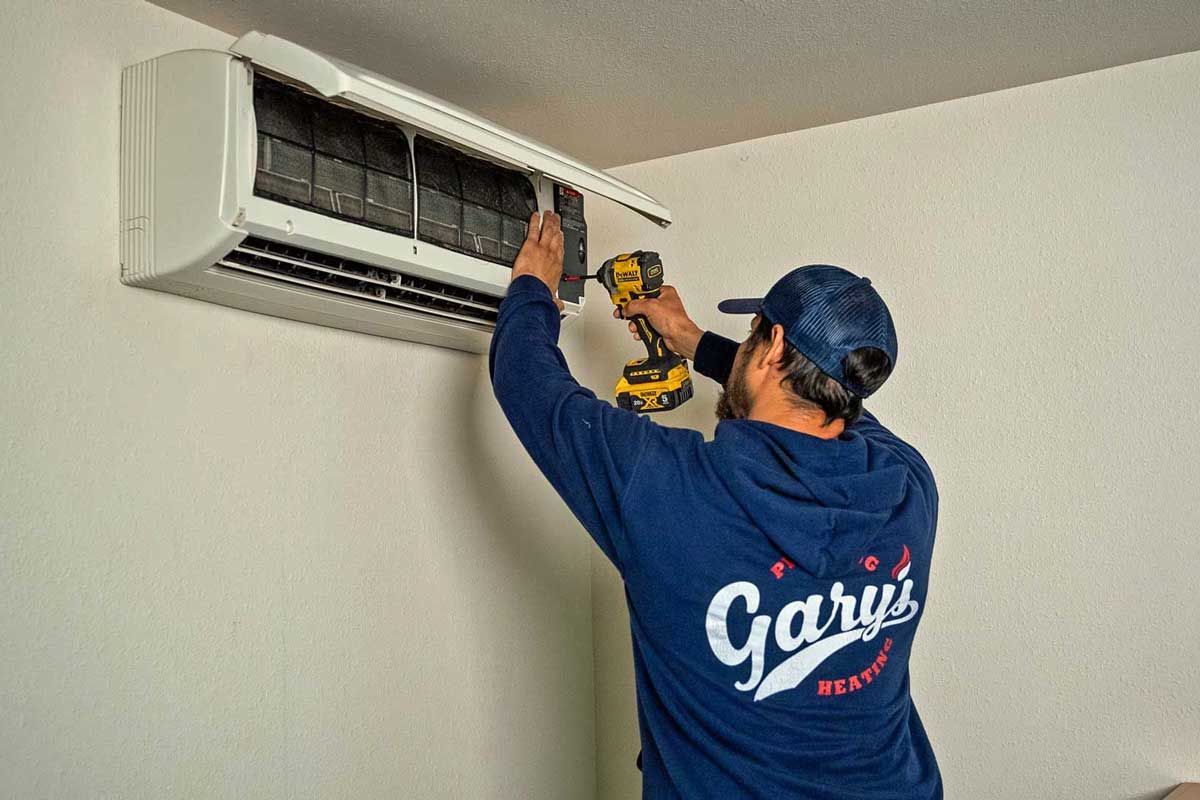 A Gary's HVAC technician is working on a mini-split air conditioner with a drill.