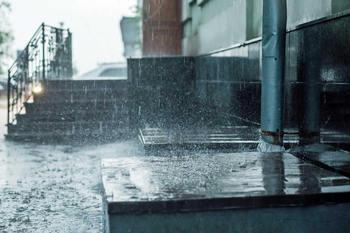 Rain is falling on a sidewalk in front of a building.