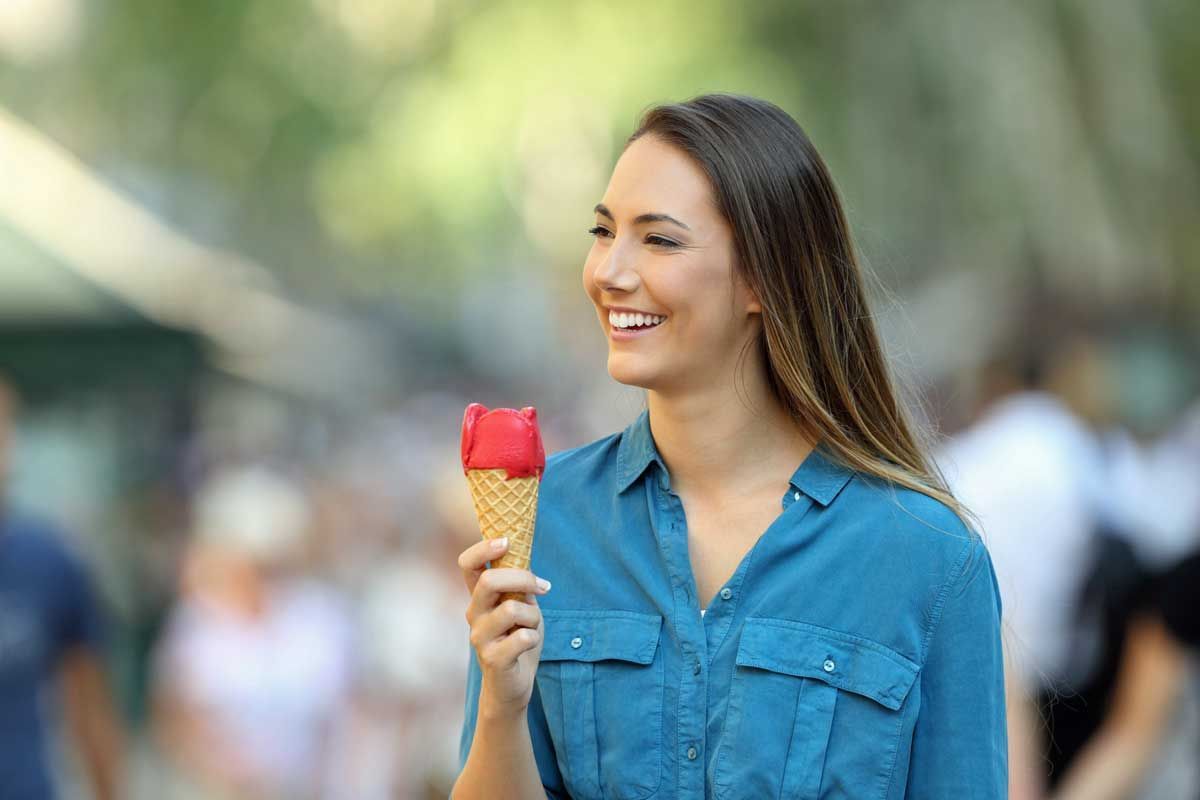 A woman is eating an ice cream cone on the street.