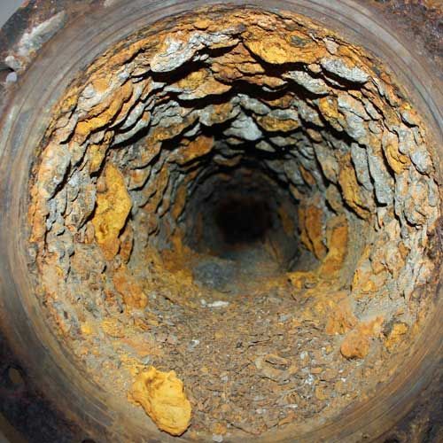 Inside of corroded metal pipe, thick layers of rust and deposits narrowing the opening.