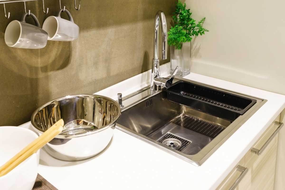 A modern kitchen sink with a pot and spoon on the counter