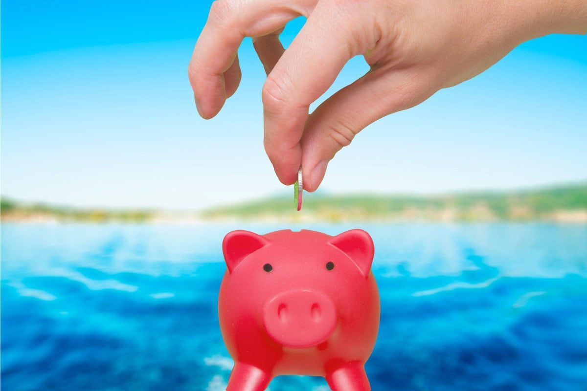 A person is putting a coin into a red piggy bank with a warm summer background