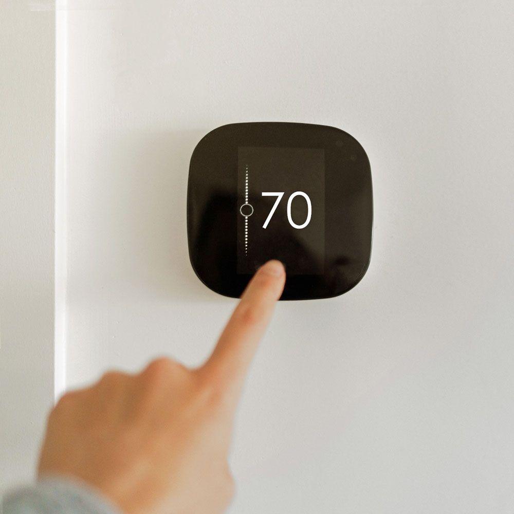 A person is pressing a button on a thermostat that says 70