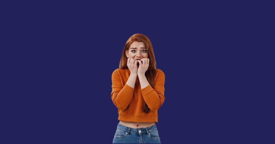 A woman in an orange sweater is biting her nails on a blue background.