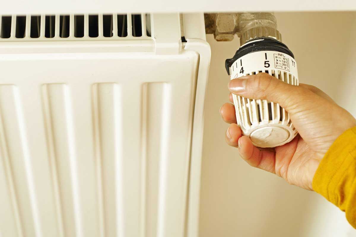 Hand turning a radiator thermostat low to prepare plumbing for vacation home absence.