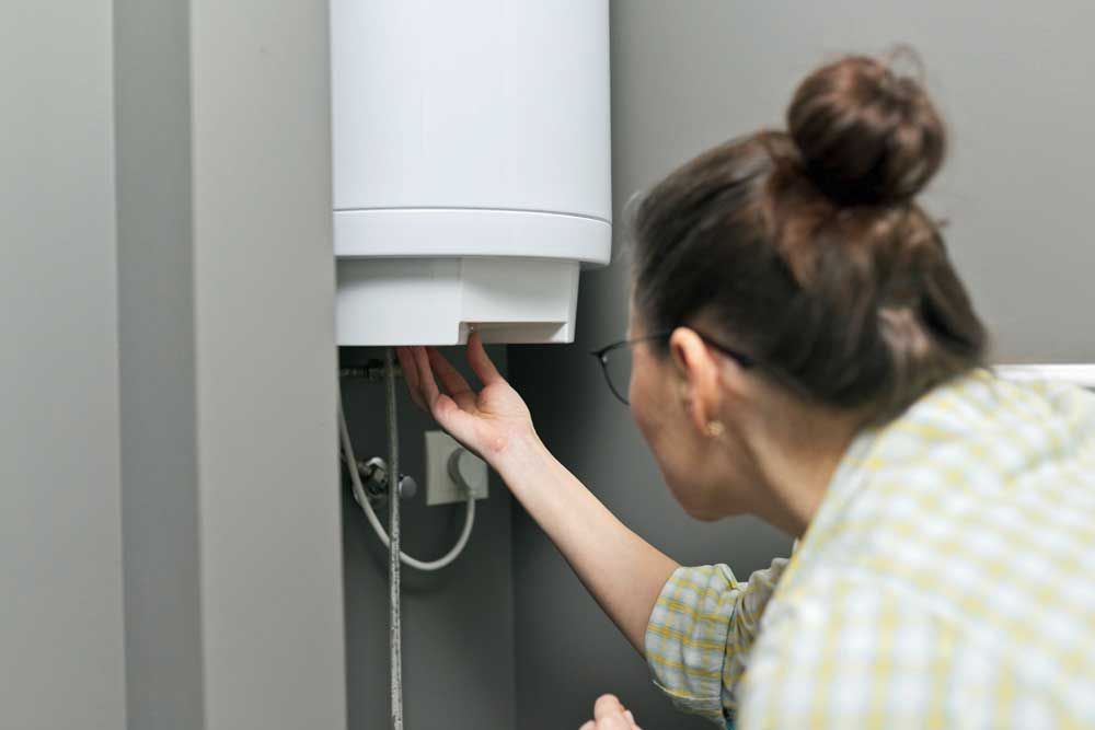 A woman is fixing a water heater in a bathroom.