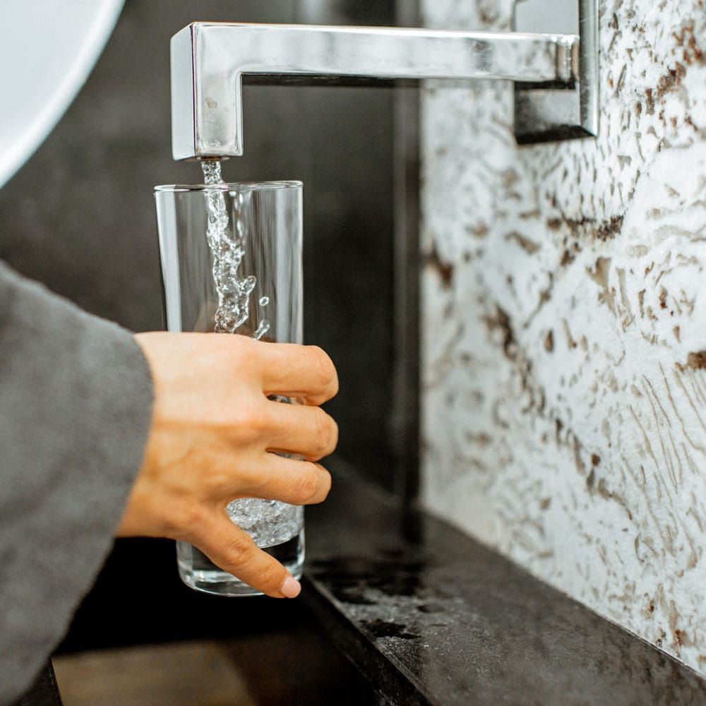 A person is pouring water into a glass from a faucet.