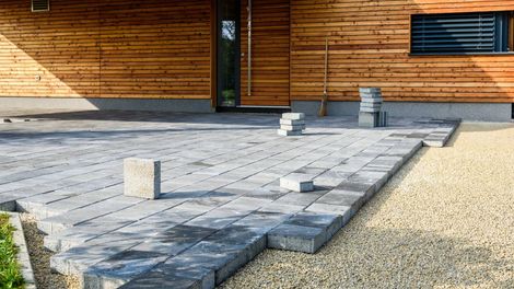 Brick paving construction in front of a wooden building. Paving stones are gray.