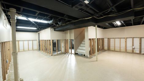 Interior of unfinished basement with exposed studs, white walls, and black ceiling.