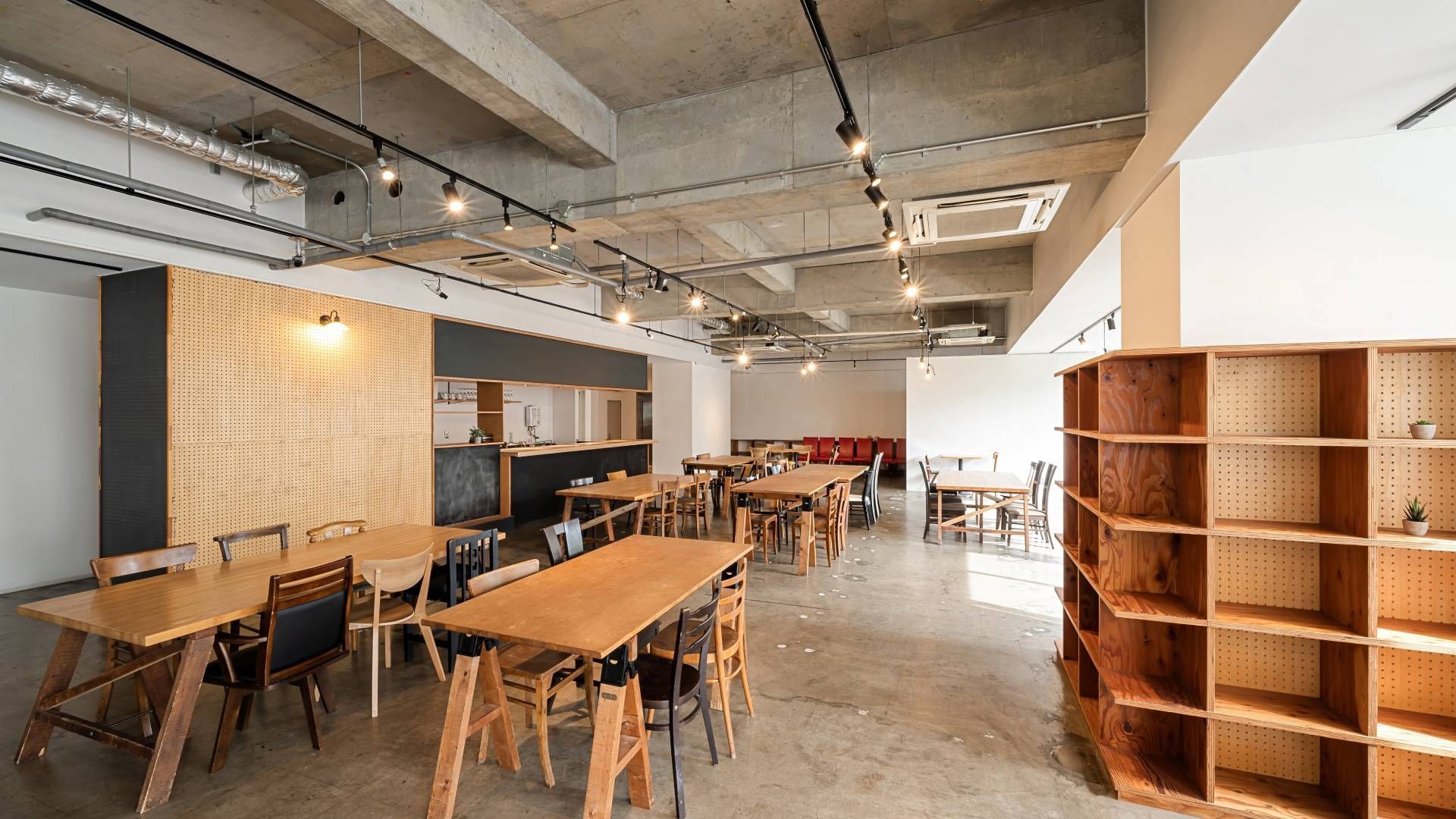 A modern cafe with wooden tables, shelves, and a pegboard wall under industrial ceiling.