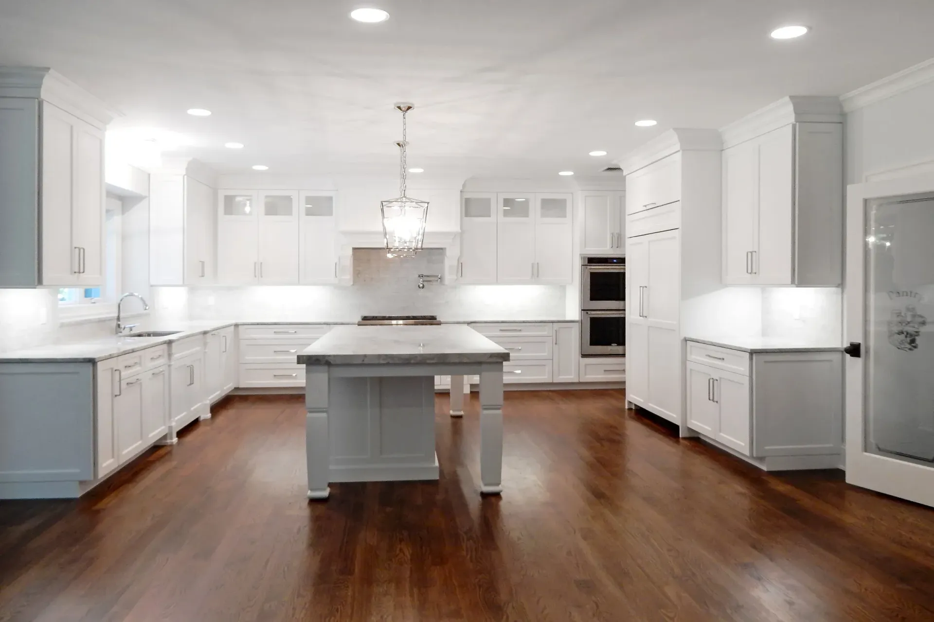 Bright white kitchen with dark wood floors, island, and appliances.