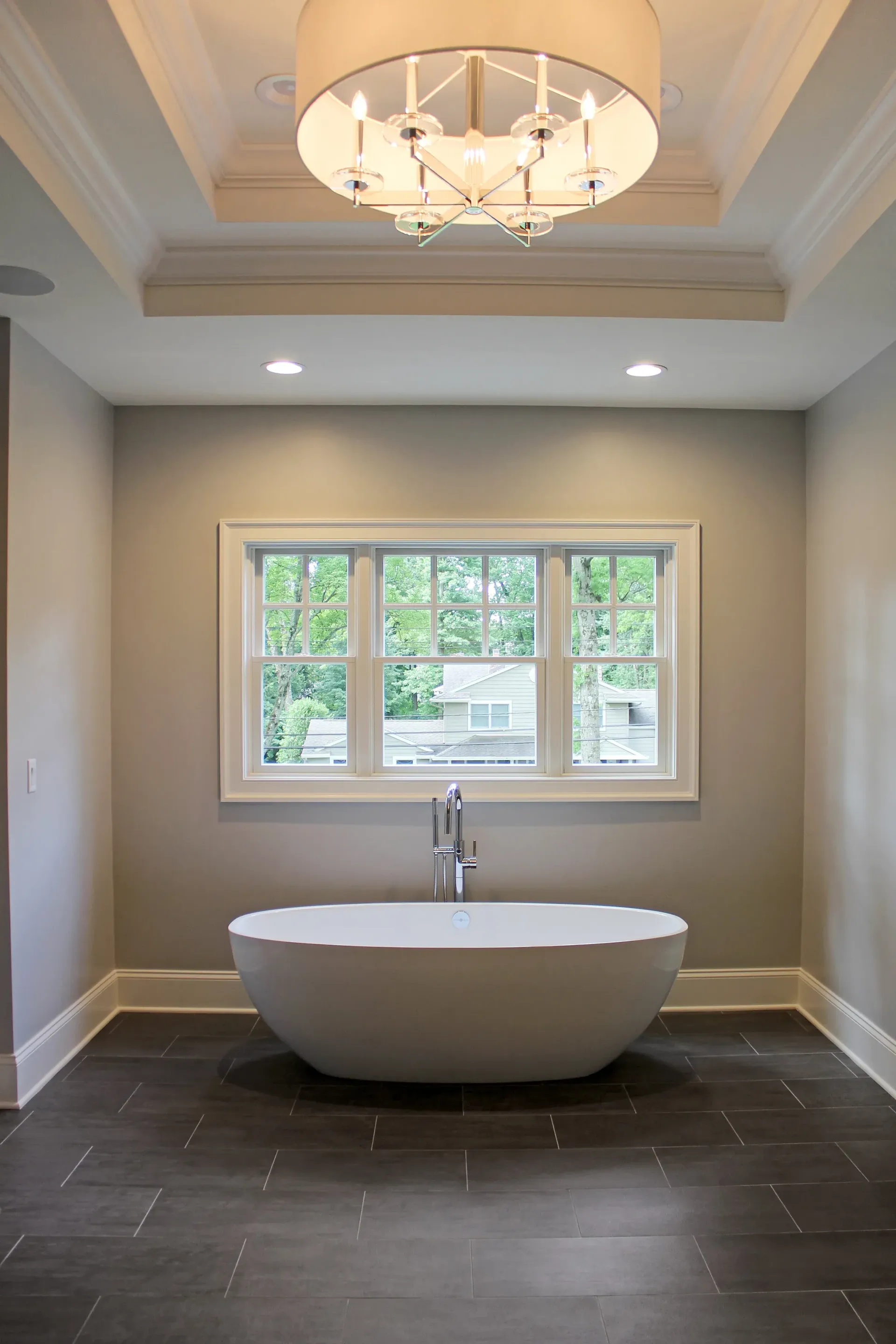 Modern bathroom with a freestanding tub, window, and chandelier.