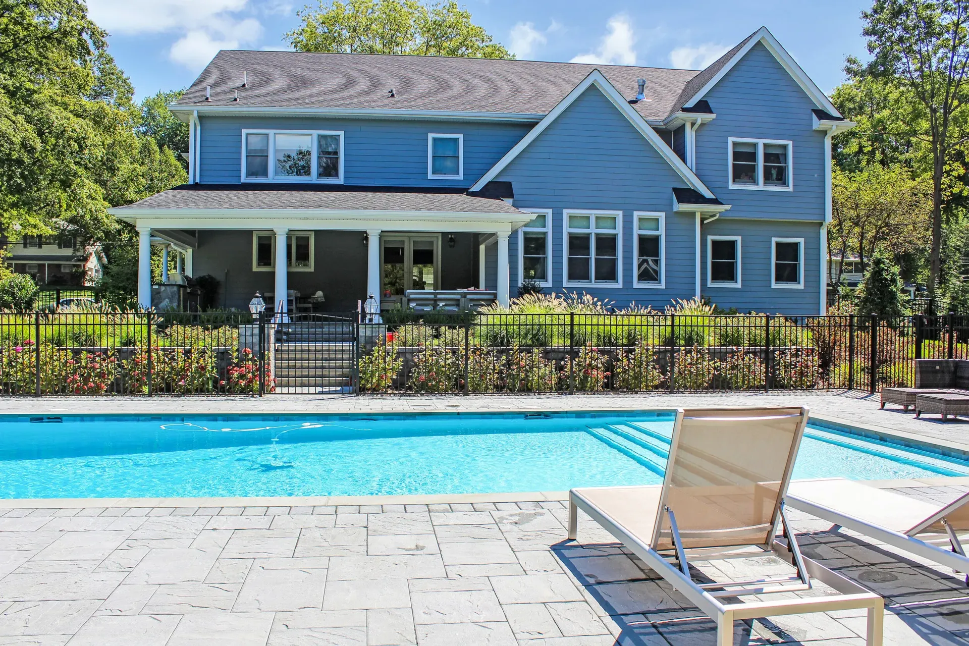 Blue house with a pool, fence, and lounge chairs.