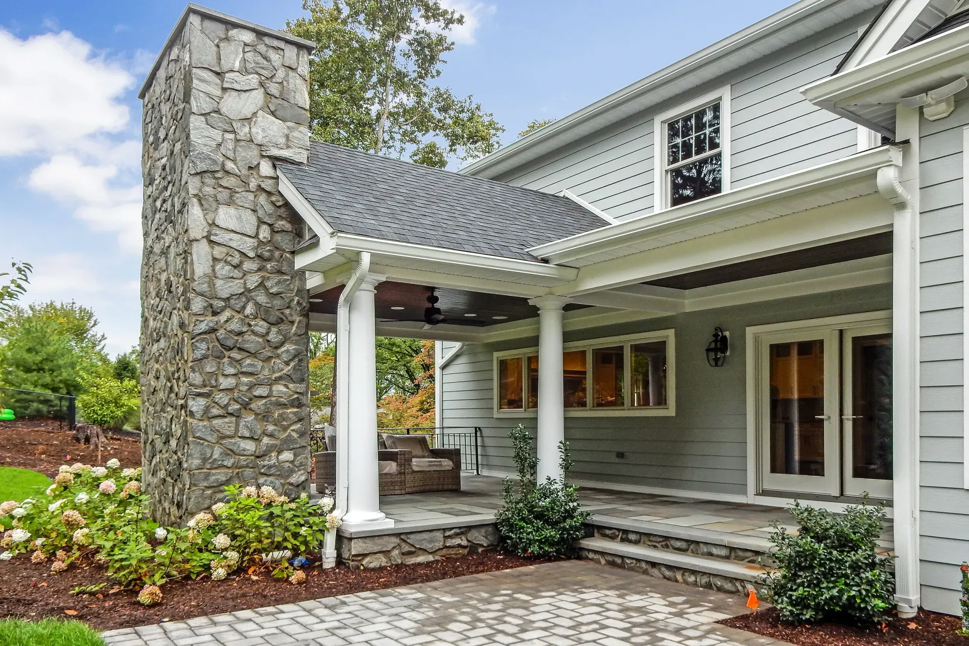 Gray house with stone chimney, covered porch, and landscaping.