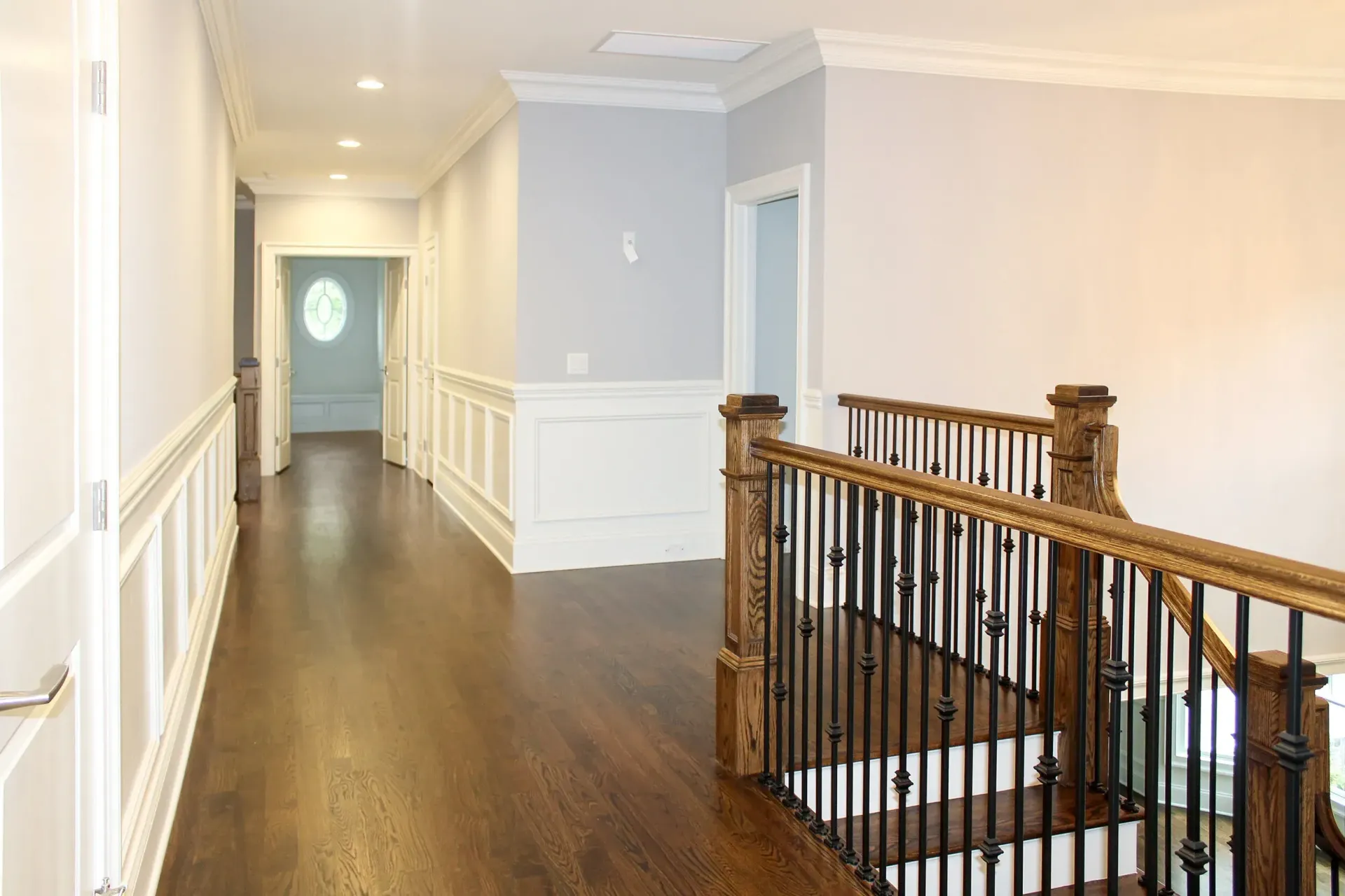 Hallway with wood floors, white trim, and a staircase with black railing and brown handrail.